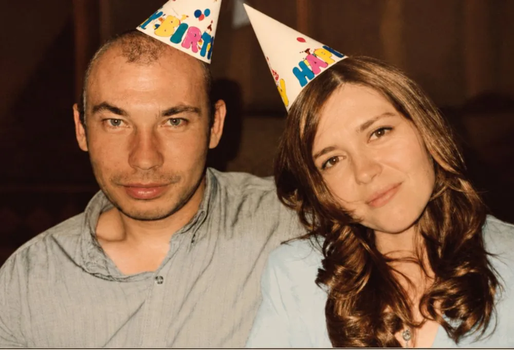 An illustration of a couple sitting close together, both wearing birthday party hats